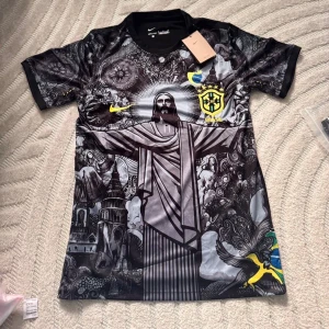 Nike Brasil fotbollströja svart/grå - Unik Brasilien fotbollströja från Nike med svart och grått konstnärligt tryck av Kristusstatyn och brasilianska symboler. Kortärmad modell med gula detaljer och CBF-emblem på bröstet. Perfekt för dig som vill sticka ut på match eller träning.