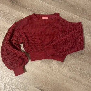 Vinröd croppad stickad tröja Signature8 - Säljer en vinröd croppad stickad tröja från Signature8 i storlek XS. Tröjan har ballongärmar, ribbade muddar och en snygg offshoulder-detalj på ena axeln. Perfekt för dig som vill ha en trendig och unik look med lite edge.