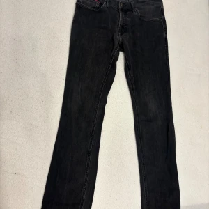 Svarta Tommy Jeans Scanton Slim - Svarta jeans från Tommy Jeans, modell Scanton Slim. Snyggt smal passform med klassisk femficksdesign och diskreta detaljer. Jeansen har en mörk tvätt och är tillverkade i stretchig denim för extra komfort. Perfekt för dig som gillar stilrena och moderna jeans.