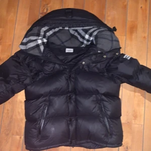 Svart pufferjacka från Burberry - Svart pufferjacka från Burberry med avtagbara ärmar så den kan användas som väst. Jackan har dragkedjor på fickorna, knappar framtill och klassiskt rutigt foder i huvan. Perfekt för kalla dagar och har en riktigt schysst streetstil. Priset kan sänkas en liten del om du är intresserad i att köpa och skriv till mig om du har fler frågor😄! Den har absolut inga problem, säljer den pga att jag behöver pengarna just nu.