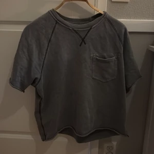 Grå kortärmad tröja Acne Studios - Säljer en chill grå kortärmad tröja från Acne Studios i 100% bomull. Tröjan har en enkel bröstficka, råa kanter och kontrastsömmar som ger en avslappnad vibe. Perfekt för dig som gillar minimalistisk stil och vill ha något som funkar året runt.