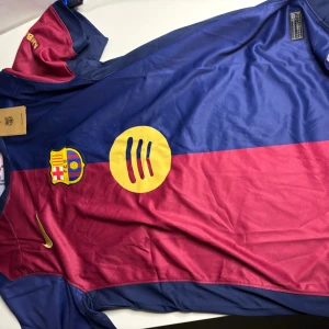 FC Barcelona matchtröja Nike blå/röd - FC Barcelona matchtröja från Nike i blått och rött med klubbmärke på bröstet, gul Nike-logga och UNHCR-tryck på ryggen. Tillverkad i lätt Dri-FIT polyester som andas. Klassisk design med korta ärmar och rund hals.