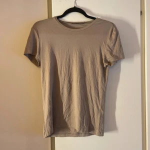 Beige basic t-shirt i bomull - Enkel och stilren beige t-shirt med rund hals och korta ärmar. Perfekt att matcha med jeans eller shorts för en clean look. Tillverkad i mjuk bomull som känns skön mot huden.