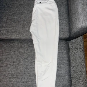 Vita mjukisbyxor med dragkedja - Snygga vita mjukisbyxor med elastisk midja och en liten dragkedja framtill. Byxorna har en normal passform och är tillverkade i mjukt material som känns skönt mot huden. Perfekta för chill dagar eller när du vill vara bekväm.