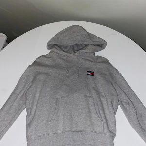 Grå hoodie Tommy Jeans med huva - Grå hoodie från Tommy Jeans i storlek S. Klassisk design med huva, snörning och magficka. Använd 1 gång.