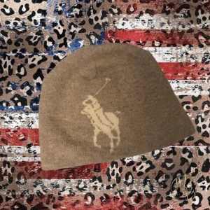 Unik Polo Ralph Lauren Mössa - Snygg beige mössa från Polo Ralph Lauren med klassisk polospelare i ljusbeige framtill. Tillverkad i mjuk lammull med skön polyesterfoder på insidan. Perfekt för dig som vill ha en stilren och varm mössa med ikonisk logga. Sjukt fräsch!