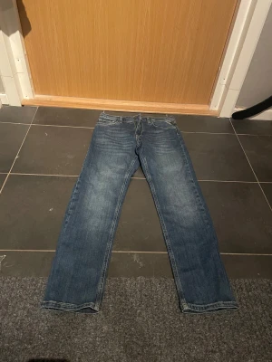 Blå Replay jeans SUBJEY 14A - Snygga blå jeans från Replay, modell SUBJEY, med klassisk femficksdesign och raka ben. Jeansen har tydliga kontrastsömmar och ett brunt Replay-märke bak i midjan. Passar dig som gillar stilrena och tidlösa jeans med skön passform.