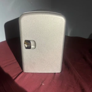 Mini kylskåp - Smidigt mini kylskåp i silverfärg, perfekt för kontor, sovrum eller resor. Kompakt design med enkel dörröppning och ventilerad baksida. Invändigt rent och utan synliga skador. Fungerar som kyl och håller drycker eller snacks kalla. Mindre tecken på normalt bruk.