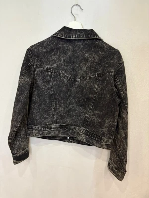 Svart tvättad jeansjacka från H&M - Snygg svart jeansjacka med tvättad look från H&M. Klassisk modell med krage, bröstfickor med lock och silverfärgade knappar framtill. Jackan har lång ärm och markerade sömmar som ger en cool vibe. Perfekt att slänga över en hoodie eller t-shirt.