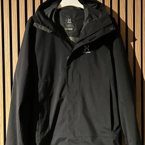 Svart Höglöfs vindjacka - Säljer min svarta höglöfsjacka som passar perfekt till allt från att åka skidor eller vandra eller bara ha allmänt. Nypris är 2400kr och den är o extremt bra skick med inga skador. Priset går självklart att diskutera!!
