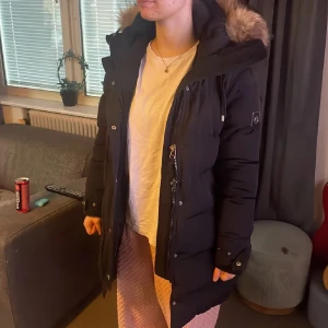 Hollies Subway - Säljer en svart dunjacka från Hollies Subway med fluffig päls på huvan. Jackan har lång passform, dragkedja och knappar framtill, samt snygga detaljer på ärmen. Perfekt för kalla vinterdagar och har en riktigt schysst look. Stooor o fin päls (äktra tror jag) Skönaste varmaste jackan till vintern💕 Använd men fint skick utan defekter alls. Använd gärna köp nu
