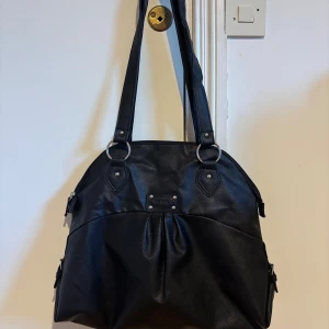 Svart axelväska från Infinity - Stilren svart axelväska från Infinity i skinnimitation med silverfärgade metalldetaljer och dubbla axelband. Väskan har dragkedja både fram och bak samt snygga ringar och nitar som ger en cool touch. Perfekt storlek för att få plats med allt du behöver.