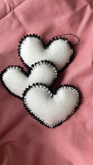 Set med 3 handgjorda hjärtan 🤍 vitt tyg & svarta pärlor – julpynt - Elegant och handgjort set med tre hjärtan i vitt tyg, dekorerade med svarta pärlor runt kanten 🖤🤍 Perfekta som julgranshängen, fönsterdekorationer eller små gåvor till någon du tycker om.