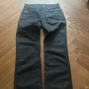 Diesel mörkblå jeans - Snygga diesel jeans i mörkblå tvätt med klassisk femficksdesign och subtila slitningar framtill. Raka ben och normal passform, perfekt för dig som gillar stilrena och tidlösa jeans. Materialet är robust denim med Replay-logga på fickan.