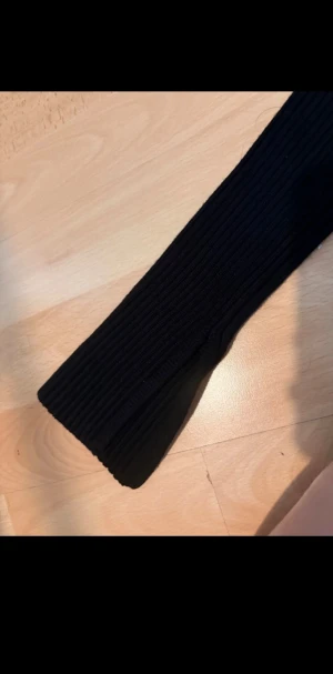 Svart ribbad stickad tröja  - Svart stickad tröja från Gina Tricot i storlek XS. Tröjan har ett ribbat mönster, rund halsringning och långa ärmar med slits. 