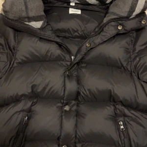 Svart Burberry puffer  - Svart pufferjacka från Burberry. Jackan har dragkedja och knappar framtill, två sidofickor med dragkedja och en huva med rutigt foder. Perfekt för kalla dagar nu i vintern. Jackan kan göras till en väst och den är i storlek M men kan även passa S. Priset kan diskuteras!