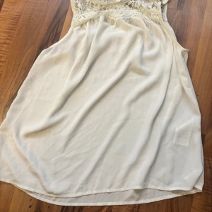 Vit spetslinne från Vero Moda - Supersöt vitt lime från Vero Moda med ärmlös design och vacker spets upptill. Linnet har en flowy passform och knäppning i nacken. Perfekt för sommarens alla tillfällen och ger en romantisk vibe.