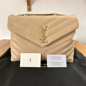 Beige ysl Loulou bag - Säljer min Yves Saint Laurent Loulou bag i beige. Den är köpt från StockX i mars 2024 och har sedan dess nästan bara legat i min garderob.  Kommer från ett rök och djurfritt hem och har få tecken på användning 😁  Äkthetscertifikatet finns med på bilden och ett digitalt kvitto finns att skicka till eventuell köpare.  Pris kan diskuteras, ställ gärna frågor vid intresse! 😊