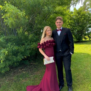 Vinröd offshoulder långklänning - Säljer en vinröd långklänning med offshoulder och volangdetaljer upptill. Klänningen har figurnära passform och en elegant, svepande kjol. Perfekt för bal eller fest. Materialet känns slätt och följsamt.