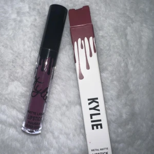 Kylie matt flytande läppstift lila - Säljer ett matt flytande läppstift från Kylie Cosmetics i en snygg mörklila nyans. Kommer i originalförpackning med svart lock och genomskinlig tub som visar färgen. Perfekt för dig som vill ha en statement-läpp med matt finish.