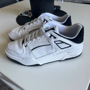 Vita sneakers från Puma - Snygga vita sneakers från Puma ”Streamline” använd 2ggr med svarta detaljer och svart häl. Skorna har klassisk snörning, rund tå och en chunky sula. Ovandelen är i skinn med texturerade partier och diskret Puma-logga på sidan. Perfekta för dig som gillar stilrena och sportiga vibes. Nypris: 1299kr !!