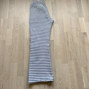 Randiga virkade byxor från Mango - Säljer ett par virkade byxor från Mango med blå ränder. Byxorna har normal midja och vida ben, vilket ger en chill och trendig look. Perfekta för dig som gillar bekväma och snygga plagg med lite retrovibbar.