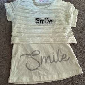 Vit topp och linne med glittertext Smile - Tvådelat set från Peri Masalı med en vit kortärmad topp i mesh med vågiga ränder och glittrig Smile-text samt ett matchande vitt linne med silvrig Smile-tryck. Perfekt för dig som gillar söta och lekfulla detaljer.