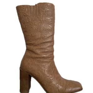 Bruna boots med mönster från Ocaia - Snygga bruna boots från Ocaia med präglat blommigt mönster i skinn. Modellen har en fyrkantig tå, blockklack och dragkedja på sidan för enkel påtagning. Perfekt för dig som vill sticka ut med coola detaljer och unik design! 💞👢