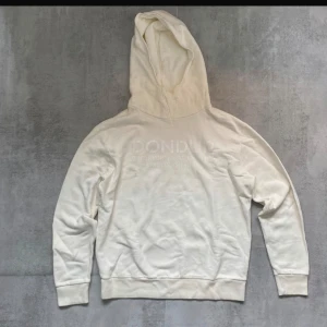 Dondup hoodie  - Säljer en stilren vit hoodie från Dondup med diskret tryck på bröstet. Tröjan är i 100% bomull, har huva och ribbade muddar vid ärmslut och nederkant. Perfekt för dig som gillar en clean och enkel look. Riktigt bra skick!