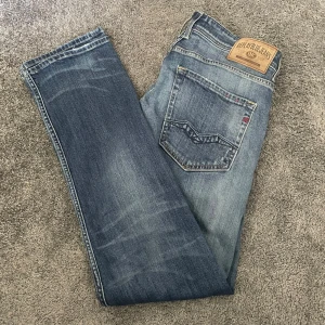 Blå Replay jeans straight fit - Säljer ett par klassiska blå jeans från Replay i rak modell. Jeansen har snygga slitningar och ljusare partier framtill, fem fickor och tydliga Replay-detaljer på bakfickan och läderpatch i midjan. Hör av er vid frågor eller funderingar. Del av Replay Rocco Comfort Fit linjen och original pris är 1299 kr.