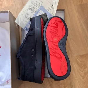Christian Louboutin svarta sneakers - Snygga svarta sneakers från Christian Louboutin i mocka med klassisk röd sula och diskreta detaljer. Skorna har rund tå, platt sula och svarta snören. Perfekta för dig som vill ha en lyxig och stilren look med en ikonisk touch.
