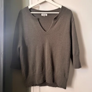 Grå v-ringad stickad tröja Soft Goat - Mysig grå stickad tröja från Soft Goat med v-ringning och trekvartsärm. Tröjan har ribbade muddar vid ärmslut och nederkant, och är tillverkad i mjuk kashmir. Perfekt för lager-på-lager och chill dagar. 