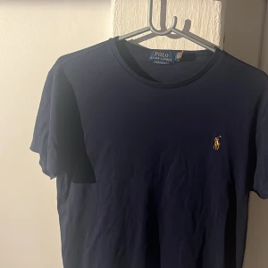 Mörkblå t-shirt från Polo Ralph Lauren - Snygg mörkblå t-shirt från Polo Ralph Lauren med klassisk gul broderad logga på bröstet. Modellen är custom slim fit. Skriv vid frågor!