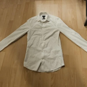 Vit skjorta från H&M i bomull XS - Klassisk vit skjorta från H&M i premium bomull. Skjortan har lång ärm, knappar framtill och en stilren krage. Perfekt för dig som gillar en clean och enkel look. Passar dig som vill ha en tidlös bas i garderoben.