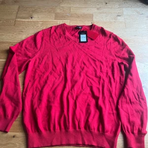 Röd v-ringad tröja i pima bomull XL - Röd v-ringad tröja från Pima Cotton i storlek XL. Tillverkad i mjuk och skön pima bomull med ribbade muddar vid ärmslut och nederkant. Perfekt för dig som gillar klassisk stil med en färgstark touch.