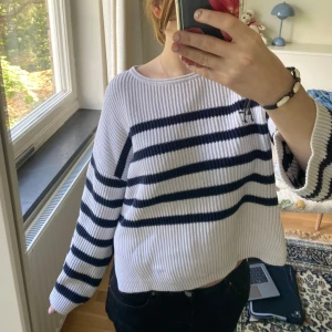 Randig vit och marinblå stickad tröja - Säljer en ribbstickad tröja i vitt med marinblåa ränder. Tröjan har en loose passform, vida ärmar och slits i sidorna. Perfekt för dig som gillar en chill och stilren look. Supermjuk och skön att ha på sig.