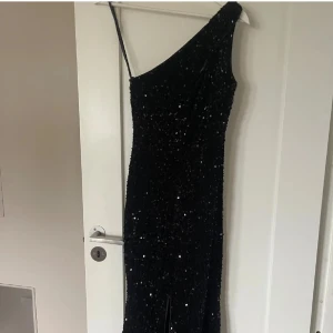 Svart glittrig långklänning oneshoulder - Supersnygg svart långklänning med glittriga paljetter och en axelbandslös design. Perfekt bakgrund balklänning