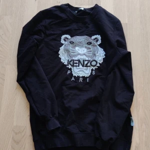  Kenzo sweatshirt - Svart sweatshirt från Kenzo med ikonisk broderad tiger och logga på bröstet. Tröjan har rund hals, långa ärmar och ribbade muddar. Perfekt statement-plagg för dig som vill sticka ut med stilren design och coolt broderi.