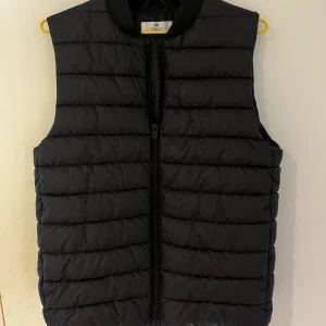 Väst H&M - Svart dunväst från H&M med rak passform och ribbad krage. Perfekt att slänga över en hoodie för extra värme. Storlek 158/164. Hör av dig vid funderingar! Mvh Carl