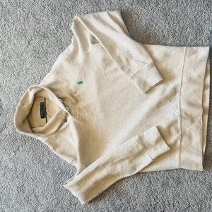 Beige hoodie från Polo Ralph Lauren - Snygg beige hoodie från Polo Ralph Lauren med klassisk grön broderad logga på bröstet. Tröjan är i mjuk bomull, har huva med snörning och långa ärmar. Perfekt för en chill och stilren look.
