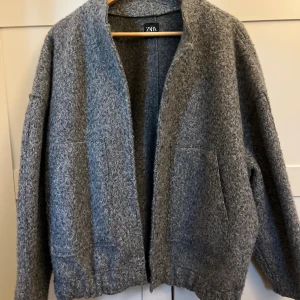 Grå teddyjacka från Zara M-L - Mysig grå ”bomberjacka” från Zara i storlek M-L. Jackan har en fluffig struktur, stora fickor framtill och stängs med tryckknappar. Perfekt för alla outfits och as snygg nu till hösten! 