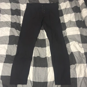 Svarta leggings med snörning från Bik Bok - Svarta leggings från Bik Bok Balance med snygg snörningsdetalj framtill i midjan. Stretchigt material som sitter tight och formar sig efter kroppen. Perfekta för en trendig och bekväm look. Storlek M.