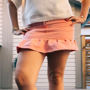 Rosa volangkjol i jeans - Supersöt kort rosa kjol i jeansmaterial med volangkant längst ner. Kjolen har klassiska fickor både fram och bak samt dragkedja och knapp framtill. Perfekt för dig som gillar färg och vill sticka ut lite extra under varmare dagar.