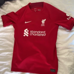 Liverpool tröja Nike - Liverpool FC matchtröja från Nike med Alexander-Arnold och nummer 66 på ryggen. Röd med vita tryck, kortärmad och tillverkad i Dri-FIT-material som andas. Klassisk passform med klubbmärke och sponsorlogga framtill.