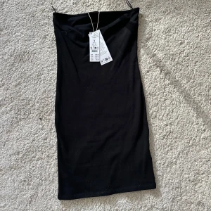 Svart tubklänning i stretch - Säljer en oanvänd svart, tight tubklänning i superstretchigt material med prislappen kvar. Köpte för 300kr säljer för 199kr. Klänningen är kort och ärmlös med en enkel, stilren design som sitter figurnära. Perfekt för dig som gillar minimalistisk och trendig stil.