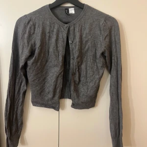 Grå kofta från H&M Divided XS - Mysig grå kofta från H&M Divided i storlek XS. Klassisk modell med rund halsringning, knappar framtill och ribbade muddar. Inte använt många gånger.