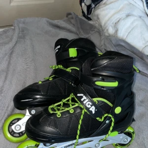 Svarta och limegröna inlines Stiga - Säljer ett par svarta inlines från Stiga, modell Tornado, med justerbar storlek 38-41. Skorna har limegröna detaljer och snören, samt robust aluminiumram och fyra hjul per sko. Perfekta för dig som vill cruisa runt med stil och komfort.