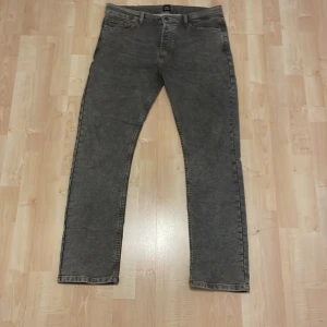 Grå jeans från Montén, rak modell - Säljer ett par grå jeans från Montén i rak modell. Jeansen har klassisk femficksdesign, snygga kontrastsömmar och en unik tvättad look. Bakfickorna har en cool zigzag-detalj. Perfekta för dig som gillar stilrena och bekväma jeans.