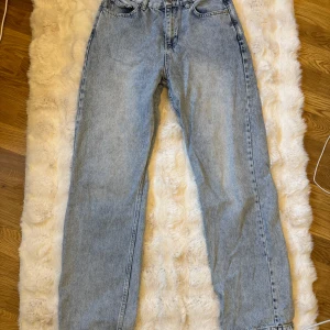 Junkyard Straight Off Jeans - Säljer ett par ljusblå jeans med klassisk femficksdesign och raka ben. Jeansen har normal midja och är tillverkade i ett mjukt denimtyg som ger en avslappnad vibe. Perfekta för dig som gillar en enkel och tidlös look.