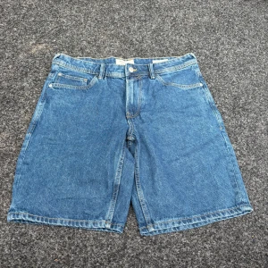 Blå loose fit jeansshorts Tom Tailor - Snygga blå jeansshorts från Tom Tailor i loose fit-modell. Klassisk femficksdesign, bälteshällor och dragkedja med knapp. Perfekta för en chill sommarstil och tillverkade i slitstarkt denimtyg.